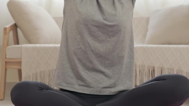 自宅でヨガを練習しながら 脚と腕を組んで運動マットの上に座っている女性のティルトアップショット — ストック動画