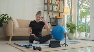 Female fitness instructor in wireless earphones waving and speaking via video call laptop while training online from home