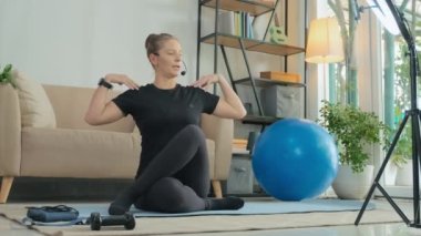 Female yoga instructor explaining how to do asana on smartphone camera held by tripod with ring light while giving online class from home