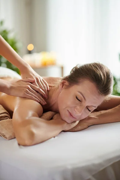 Mature woman enjoying getting shoulder massage in salon to get rid of stress and anxiety