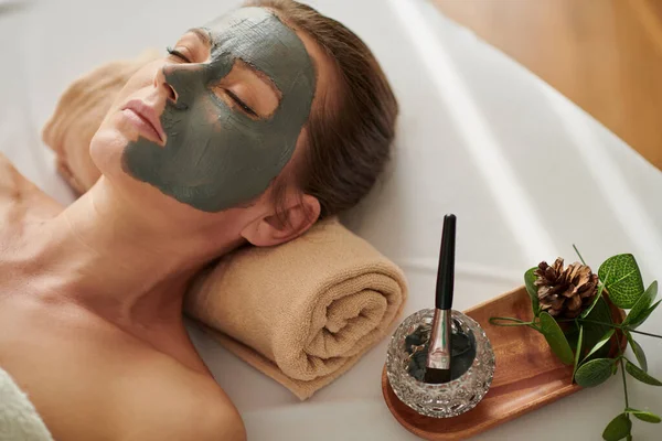 Relaxed woman with clay mask on half of her face
