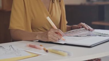 Cropped shot of female designer coloring fashion illustrations with felt tip pen while working on new clothes collection