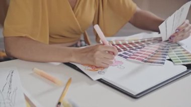 Cropped shot of female designer coloring fashion sketches with felt tip pen while creating new collection
