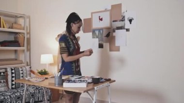 Creative African American woman making paper collage in frame hanging as decorative picture on wall in art studio