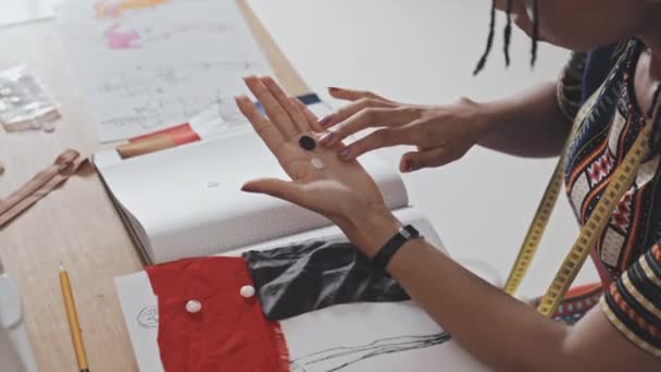 缝纫车间的非洲裔美籍女裁缝师近照 脖子上缠着测量带 在桌子上选择纽扣 — 图库视频影像