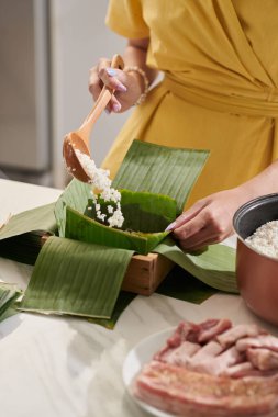 Closeup image of woman putting rice on banana leaves when cooking for Tet