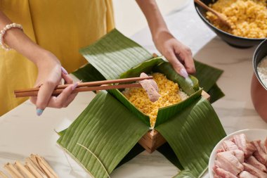 Hands of woman putting pieces of marinated pork inside sticky rice cake