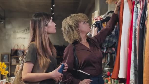 2人の若い女性の中から服を選び ブティックストアで一緒に買い物をしながらそれについて話し合う — ストック動画