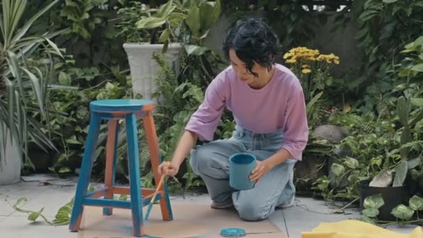 庭で屋外古い家具を復元しながら 青塗料とジェンZの女の子の絵画スツールの中長期ショット — ストック動画