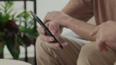 Two unrecognizable male friends scrolling on smartphone while staying at home together