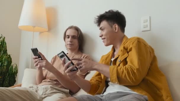 Two Buddies Early 20S Scrolling Smartphones Chatting Sitting Couch Home — Αρχείο Βίντεο