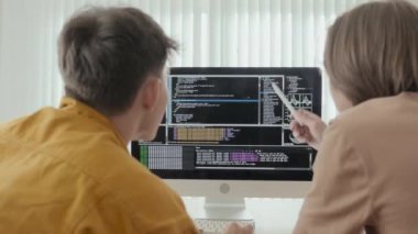 Over the shoulder shot of two male friends discussing program codes on black screen of computer monitor