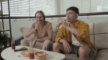 Two guys of Caucasian ethnicity getting together at home drinking beer with chips and chatting