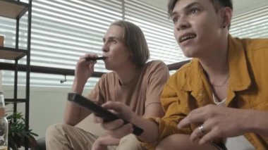 Two best mates in their early 20s chilling together at home watching TV and smoking e-cigarette