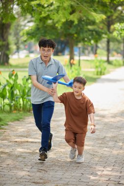 Father and son playing in park with toy airplane they created at home