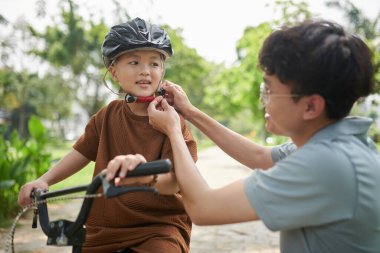 Father helping little boy to put on helmet before riding bicycle