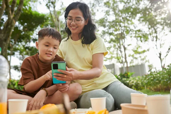 Smiling mother showing new game on smartphone to preteen son