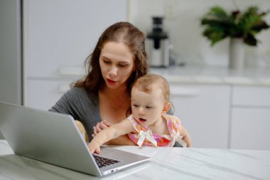 Young mother showing game on laptop to little daughter