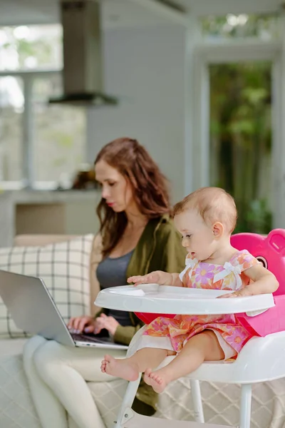 Young Woman Working Laptop Her Daughter Playing Feeding Chair — Stockfoto