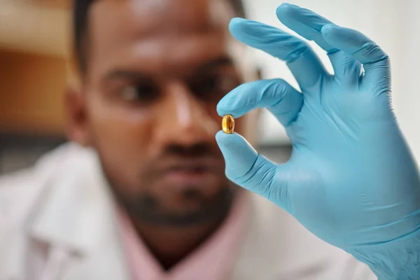 Medical scientist holding pill with fish oil, selective focus