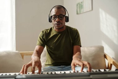 Musician in headphones playing synthesizer when composing new song for singer