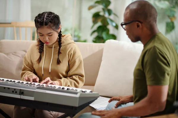 Teenage girl trying hard to play new song on synthesizer without mistakes
