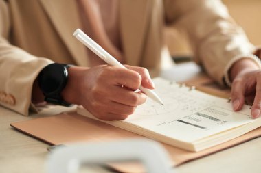 Hands of manager sketching charts in planner when getting ready for meeting