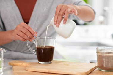 Closeup image of woman pouring cream in cup of black coffee