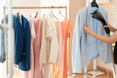 Woman steaming light blue jaket when getting ready for work