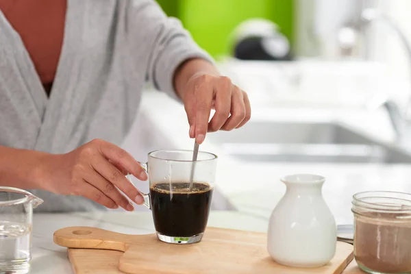 Woman mixing sugar in coffee mug on kitchen table