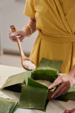 Hands of woman filling wooden mold with rice when making Banh tet cake