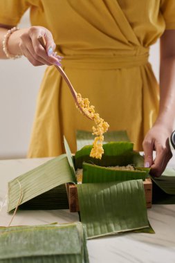 Housewife adding mung beans in mold covered with banana leaves