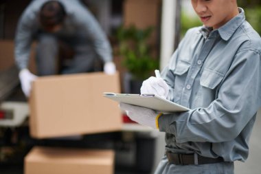 Mover filling document when his coworker loading truck in background