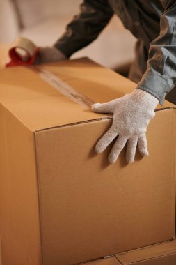 Closeup image of mover sealing cardboard box with belongings of client