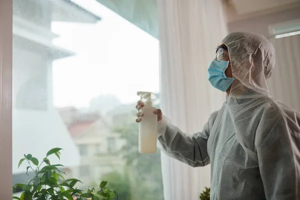 Desinfecting service worker spraying detergent on big house window