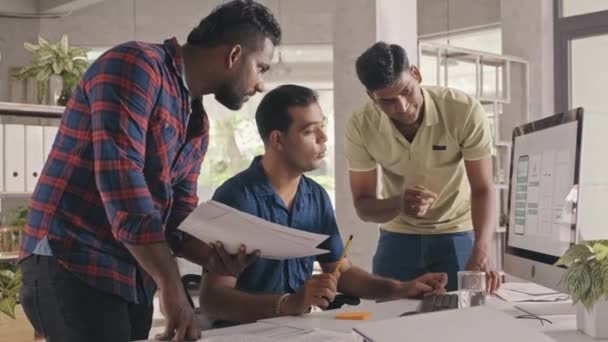 It企業のオフィスでプロジェクトを共同作業しながら 紙やコンピュータ画面上のモバイルアプリのワイヤーフレームを議論するインドのUxデザイナーのチームの中程度のショット — ストック動画
