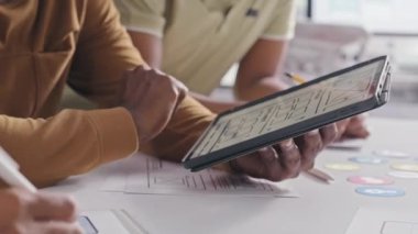 Close up shot of hands of UX designer showing digital sketch of mobile app interface on tablet while collaborating with team in office