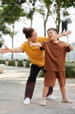 Joyful preteen boy spending time with grandmother exercising in park