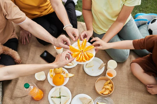 Hands of family members taking slices of orange from plate, view from above