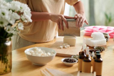 Hands of woman using metal cutter when cutting soap base in small cubes for melting clipart