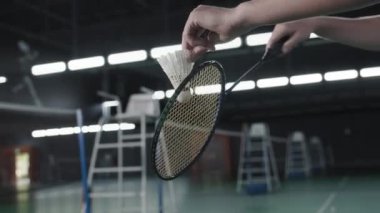 Close up arc shot of hands of unrecognizable sportsman holding shuttlecock and moving racket while training on indoor court