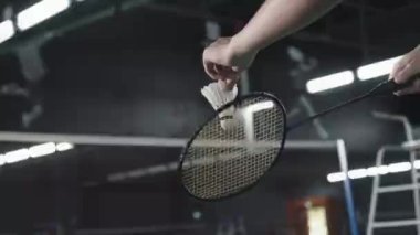 Close up low angle shot of hands of unrecognizable tennis player holding shuttlecock and racket while training on indoor court