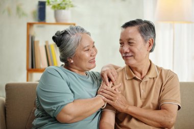 Happy senior man and woman sitting on couch and looking at each other with love and affection