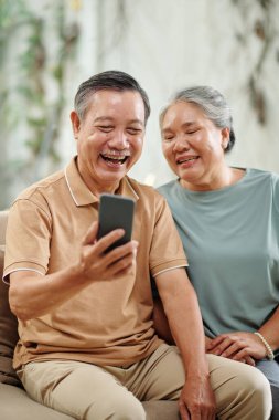 Happy senior husband and wife video calling their friends