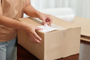 Person sticking delivery information on cardboard box before sending it