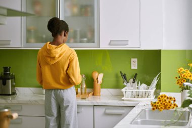 Young woman in loungewear cooking breakfast at kitchen counter, view from back