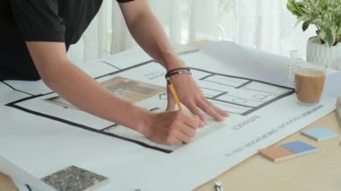 Cropped shot of male designer taking notes on apartment floor plan while working on interior project at table in office