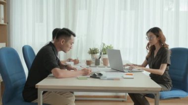 Genç Asyalı meslektaşlarının ofis masasında birlikte çalışırken planlar çizip dizüstü bilgisayar kullandıkları bir fotoğraf.