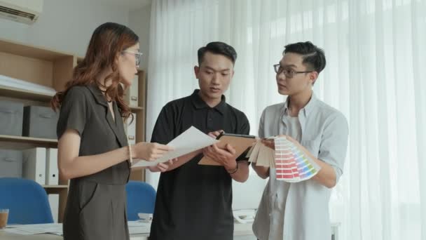 紙のプランやカラーパレットを議論しながら オフィスでプロジェクトに取り組む若いアジアのデザイナーのグループの中のショット — ストック動画