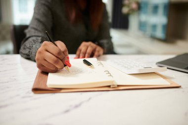 Closeup image of businesswoman writing notes in planner